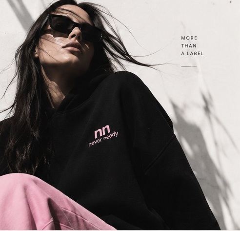 Never Needy campaign portrait in black hoodie and pink trousers